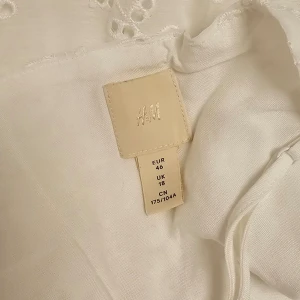 H&M klänning Anglaise - Klänning, stl. 46 (L) Vadlång klänning i luftig väv med broderi anglaise. Smala, justerbara axelband och V-ringning med insydd omlott framtill. Volangsöm i midjan, dold dragkedja i ena sidan och utsvängd kjol, Fodrad. Aldrig använd, nyskick. 
