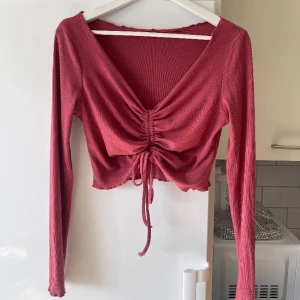 Långärmad topp - Gullig långärmad topp i typ hallon röd/rosa, stretchigt material och går att knyta så den blir kortare och mer urringad om man vill det! Använd fåtal ggr så nyskick ❤️