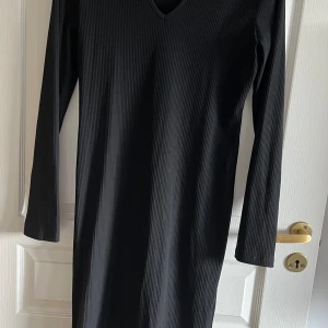 Svart enkel v-ringad klänning - Använd fåtal gånger som ny. Svart ribbat tyg, rak modell