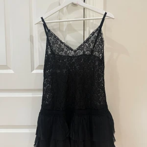 Svart miniklänning - Så snygg miniklänning med spets och volanger samt justerbara band. Originellt köpt på beyond retro men använd ca 2 gånger av mig.