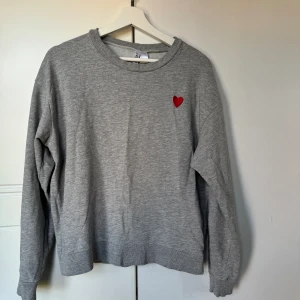 Sweatshirt grå - Grå sweatshirt med ett rött hjärta från H&M, storlek L. Sparsamt använd, inget synligt slitage. 