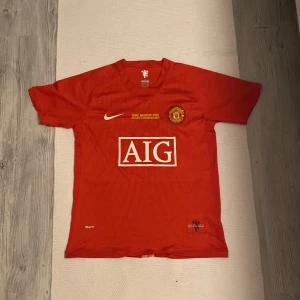 Röd Manchester United fotbollströja med Ronaldo 7 - Säljer en röd Manchester United fotbollströja från Nike i storlek herr M. Tröjan har korta ärmar och är i nyskick. Den har AIG som sponsor på framsidan och Ronaldo 7 på baksidan. Tröjan är från finalen i Moskva 2008, vilket står tryckt på framsidan.