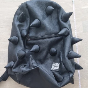 Madpax svart taggig ryggsäck - Stor ryggsäck: ca 40×28 cm. Framficka: ca 20×22 cm. Har använts några år och har lite slitage på topparna av taggarna men påverkar inte användningen. Annars i bra skick. Nypris: 700 kr. För mer info, skriv gärna✨️  