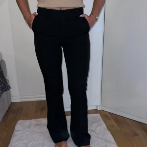 Svarta kostymbyxor - Säljer ett par svarta kostymbyxor i nyskick. De är högmidjade och har en slim passform som sitter snyggt på kroppen. Byxorna har en dragkedja och knappar framtill samt fickor både fram och bak. Perfekta för både jobb och fest!
