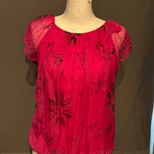 Rosa blommig blus från Position - Säljer en söt rosa blus från Position med ett blommigt mönster. Blusen har korta ärmar och en rosett vid halsen. Perfekt för sommardagar eller en festlig kväll!