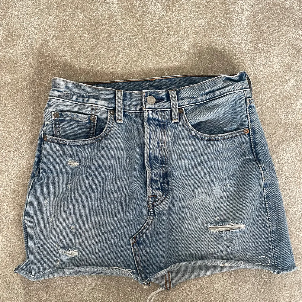 Säljer denna jeanskjol från Levi's.  Den har en cool distressed look med slitningar på framsidan och baksidan. Perfekt för sommaren! 🌞. Kjolar.