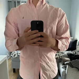 Ralph Lauren skjorta - Säljer min Rosa Oxford skjorta. Den är en lite bredare modell än den vanliga Ralph Lauren Oxford skjortan men passare perfekt till den som inte vill att skjortor sitter på tajt.