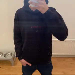 En svart hoodie med tryck på ryggen och text på framsidan 