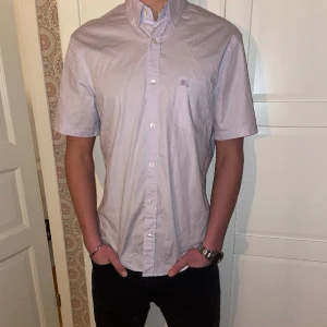 Burberry Skjorta - Säljer en äkta och riktigt fin skjorta från ”Burberry”. Skjortan är i nyskick och är bara använd ett fåtal gånger. Passar att ha en tröja över skjortan också. Skjortan är väldigt ljuslila och liknar rosa (Pris kan diskuteras). 