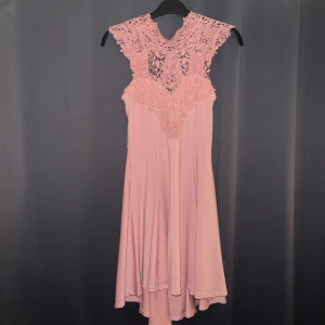 Rosa klänning från Bubbleroom - En elegant rosa klänning från Bubbleroom med spetsdetaljer på överdelen och en knytning i ryggen. Klänningen har en ärmlös design och en flödande kjol som slutar strax ovanför knäna.