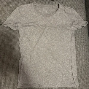 Tommy Hilfiger t-shirt - Grå bas t-shirt från Tommy Hilfiger, storlek är 152/164 cm (barnstorlek) men funkar som XS/S. Finns ett litet hål (se bilder) men det är inget som märks.
