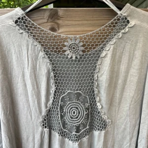 Härlig topp med virkat i ryggen  - Så härlig topp/t-shirt med vida ärmar och broderat i ryggen. Tvättat utseende, inte mycket använd i fint skick! Luftig härlig viskos. Passar stl 38-42, lite smalare nedtill och vidare upptill, lite nedhasad axel. Gråblå färg