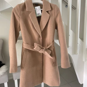 Hm kappa beige brun - Säljer denna splitternya beiga kappa från hm, fin till hösten o aldrig använd då den har prislappen kvar!