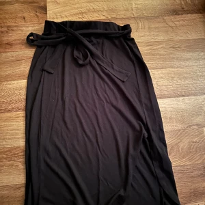 Midi kjol - En svart kjol från nakd, man knyter den vid midjan på så sätt kan man välja hur den ska sitta på, den är väldigt stretchig. Använt endast en gång, har slits längst ner i.