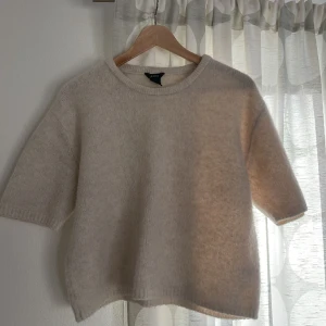 Kortärmad stickad tröja  - Stickad tröja med kort ärm i cremevit färg.  Något noppig men går enkelt att ta bort.  Lite boxig i modellen