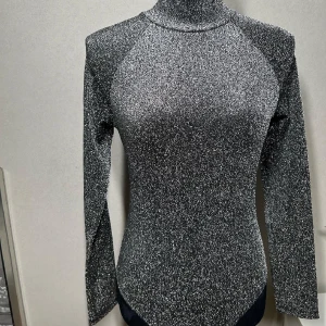 Glittrig Bodysuit  - Säljer min jätte snygga body som är svart glittrig. Köpt på Chiquelle. Skön material inuti så den sticks inte. Knäpps lätt upp. Fina detaljer på ryggen. Storlek M passar även S