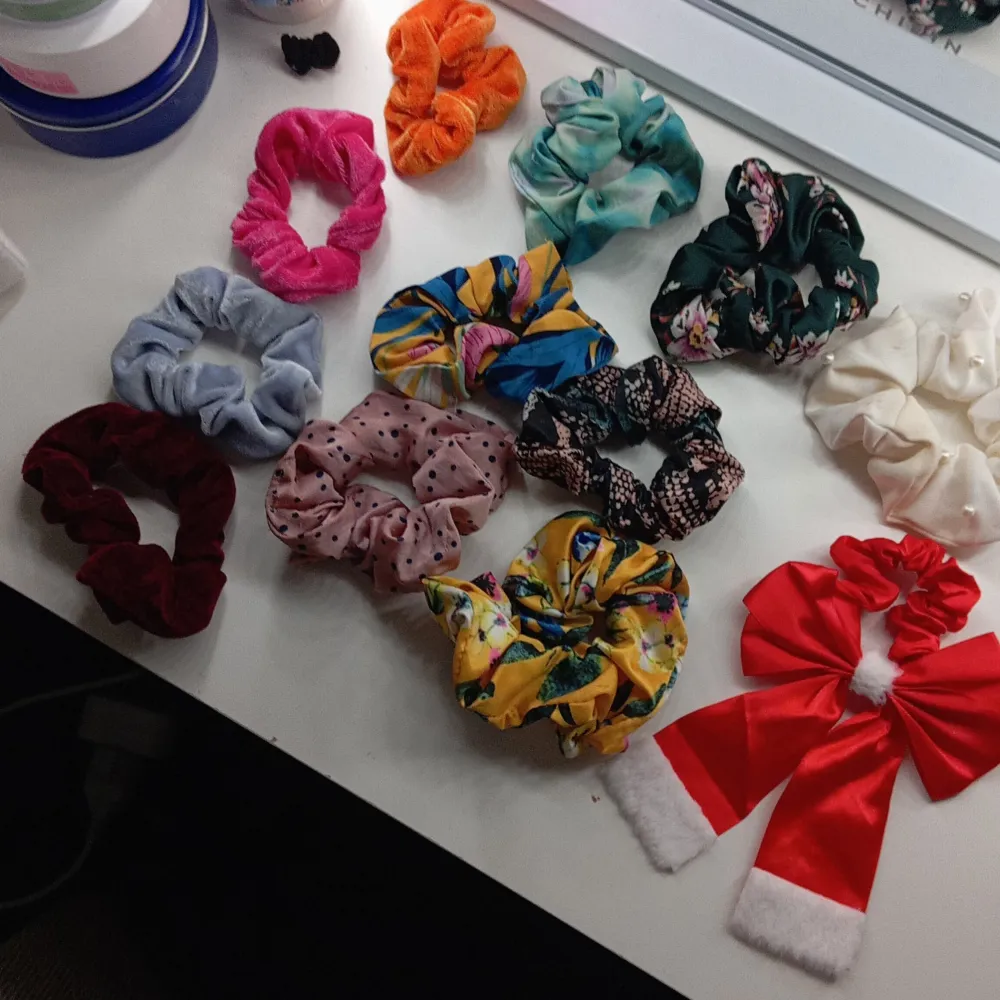 En samling av olika scrunchies i olika färger och mönster, inklusive en röd julrosett med vita detaljer. (Har två oranga). Accessoarer.