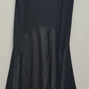 Svart klänning - En elegant svart klänning från H&M. Klänningen har en lång design och är tillverkad i ett material som ger en fin glansig effekt på den nedre delen.