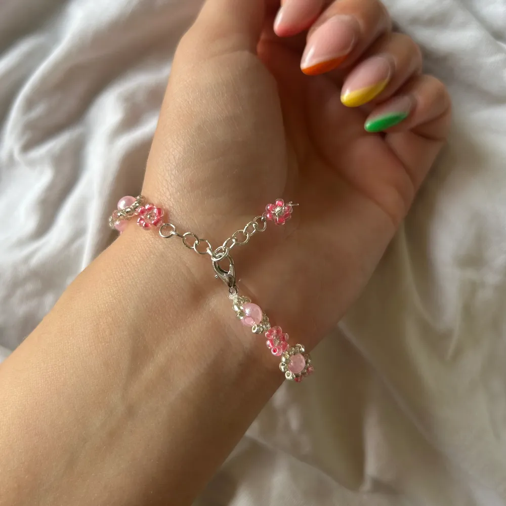 Handgjort armband med rosa blommor och silvriga/ljusrosa deltaljer. . Accessoarer.