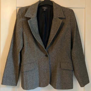 Grå mönstrad kavaj - Grå fiskbensmönstrad ullkavaj (insidan i polyester) från Mexx. I gott skick, knappt använd. Den angivna storleken är 40 men passar 36-38