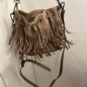 Handväska - Säljer min söta handväska med fransar 💞 den är åt det bruna hållet och ej åt det gröna som det kan se ut som i kameran. Sparsamt använd, bra fack inuti
