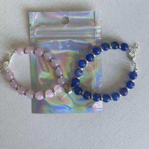 Egengjorda pärlarmband med blåa och rosa pärlor. Armbanden har en varsin berlock som avbildar ett halvt hjärta med magnet så de två armbanden kan sitta ihop. 