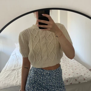 Beige stickad tröja - En beige stickad tröja med korta ärmar och ett flätmönster. Tröjan är croppad och har en ribbad kant vid ärmslut och nederkant. Storlek 38 men sitter som 36❤️