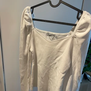 Topp med puffärm - Vit långärmad åtsittande topp med puffärm vid axlarna. Låg fyrtkantig urringning både fram och bak. Använd några gånger men är som ny, från NA-KD.💕