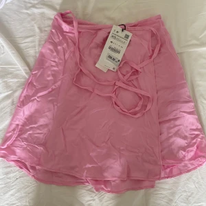 Rosa satinkjol - Helt ny med lappen kvar! Passar även S/M då den knyts omlott. Superfin men kom aldrig till användning, pris kan diskuteras💗