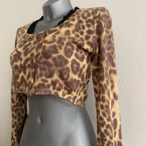 Kofta  - Fin vintage leopardmönstrad kofta med svarta spetsdetaljer vid halsen. Dubbelknäppt framtill med knappar.  Koftan är kort och har långa ärmar. Amerikansk storlek 4, passar jättebra på en S.