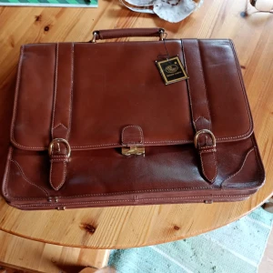 Vintage dam läderväska brun. - Vintage dam läderväska brun med Etikett kvar Lady Carlo oanvänd.Låses med tryckknappar dock fattas ett lås ,se bild.Annars i mycket fint skick.