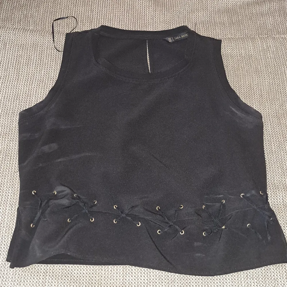 En svart ärmlös topp med snörningsdetaljer vid midjan. Toppen har en enkel design med rund halsringning och är tillverkad i ett mjukt material. använt den bara 1 fång på min födelsedag och sen det var inte längre på min storlek 🥲🥲🥲. Yläosat.