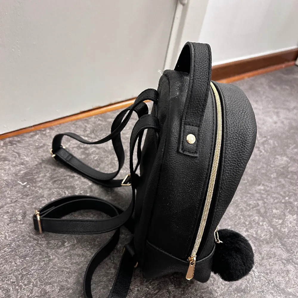 En helt ny svart mini ryggsäck med guld detaljer från hm 👛Pompom boll med följer väskan eftersom den köptes med bollen på sig men går lätt att ta av 💕 ALDRIG ANDVÄND! . Väskor.