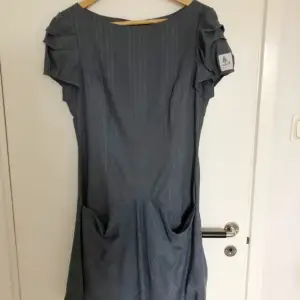 Jättefin gråblå klänning i storlek M av märket Tauko. Två stora fickor fram. Sparsamt använd, så i väldigt fint skick. Inget att anmärka på.Inga hål eller fläckar.