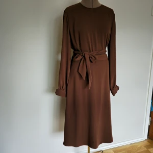 Långärmad midiklänning - Knappt använd brun midikkänning från Esprit. Lång o fin bältesdetalj för att vira runt midjan två varv, dold blixtlås bak