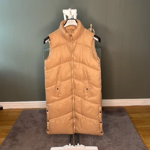 Veromoda väst  - Ärmlös, vadderad väst med hög hals, blixtlås fram och två sidofickor med tryckknappar. Bär denna coola väst över en snygg skjorta och lägg till ett par raka jeans och sneakers för en fantastisk vardagslook.