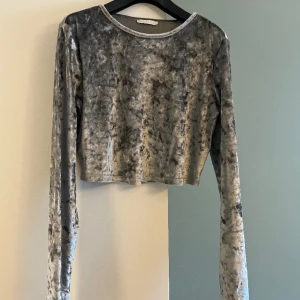 Silvertopp - En silvrig topp i kort modell med långa ärmar. Köpt på Zara, i storlek M. I bra skick, använda ca 1-3 ggr. Har ett mjukt glansigt velour-tyg. 