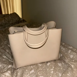 Handväska  - Beige handväska som kommer med ett axelband också. rymlig men ändå inte för stor 