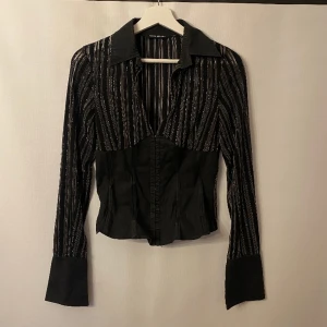 Skjorta med inbyggd korsett - En svart och silverglittrig skjorta med inbyggd korsett. De randiga tyget är lite tunnare/ mesh. Perfekt till nyår!!!  Märke: Tally Weijl. Storlek: S