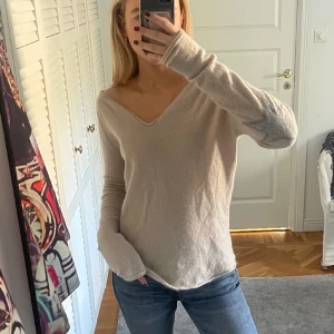 Ull tröja  - V-ringad, beige tröja från Hunkydory Essentials. Präglas av gråa stjärnor på armbågarna. Tyvärr ett litet hål vid ena axeln, går med största sannolikhet att laga själv. Nypris nästan 3000 kr. 