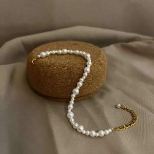 Beskrivning: Milis är ett armband som består av flera olika storlekar av vita pärlor med lås i guld och kedja i guldfärg med lack.   Namn: Milis Längd: Hela 23 cm Pärlor 16 cm