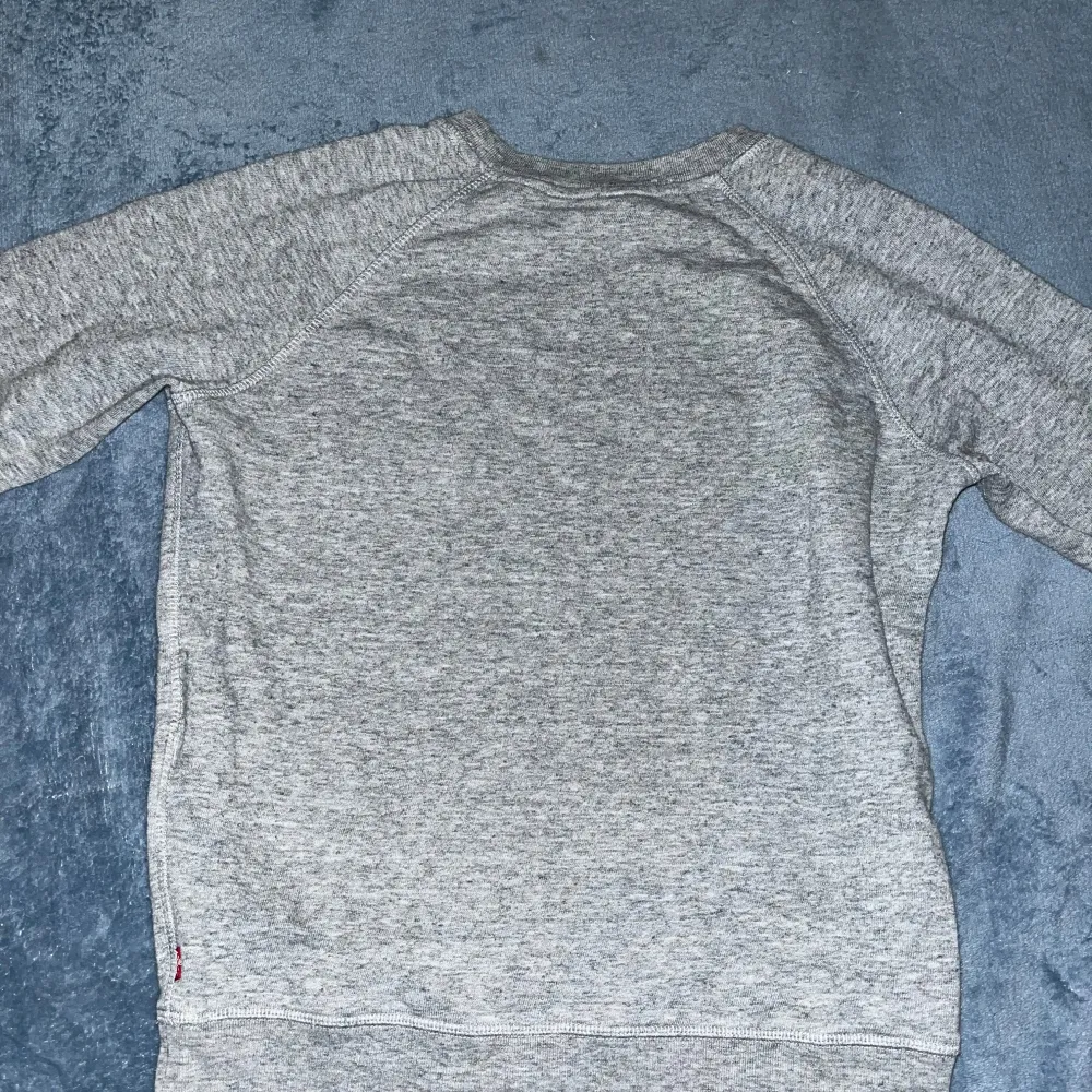 Säljer en grå sweatshirt från Levi's med deras ikoniska logga i rött på bröstet. En klassisk och stilren design som passar till det mesta.. Neuletakit & Villapaidat.