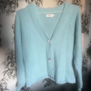 Ljusblå kofta från ONLY - Säljer en superfin ljusblå kofta från ONLY med glittriga knappar. Den har en v-ringad design och långa ärmar, perfekt för att hålla sig varm och stilren. Passar perfekt till både jeans och kjol. 💙