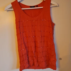 Röd paljettlinne från Lindex - Snyggt rött linne från Lindex med paljettdetaljer som ger en glittrig effekt. Perfekt för att liva upp garderoben med lite extra bling. Linnet har en rund halsringning och ärmlös design.