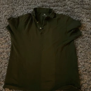 Svart kortärmad pikétröja från H&M - Snygg svart pikétröja från H&M med korta ärmar och klassisk krage. Perfekt för en avslappnad stil. Tröjan har knappar framtill för en stilren look.