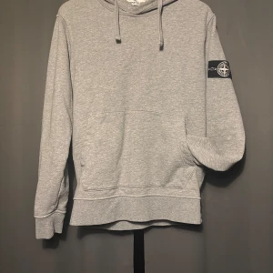 Stone Island Hoodie - Grå Stone Island hoodie i strl M, fits S. Skick; 9/10. Tillkommer en extra badge, en vit (bild 1) och en klassisk (bild 2). Skriv vid frågor och funderingar!