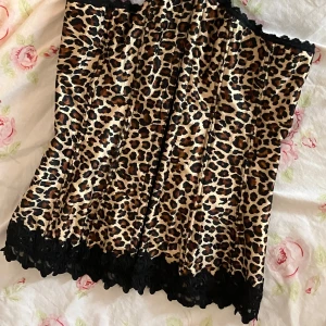 Leopard korsett - Snygg leopardmönstrad korsett från Frederick's of Hollywood med svarta spetsdetaljer och snörning framtill. Tillverkad i polyester och spandex för en bekväm passform.