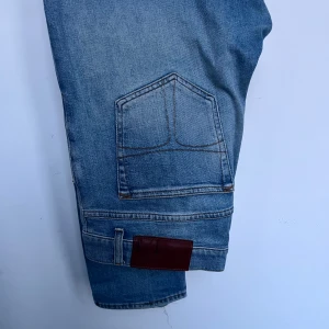 Tiger of Sweden - Snygga blå jeansbyxor med unik fickdesign och brunt lädermärke. Perfekta för en avslappnad stil.
