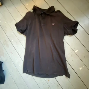 Svart pikétröja från GANT - Säljer en stilren svart pikétröja från GANT i storlek XL. Tröjan har korta ärmar och en klassisk krage med knappar. Perfekt för en avslappnad men ändå snygg look.