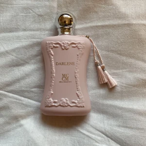 parfym - Elegant parfymflaska i ljusrosa med dekorativa detaljer och en silverfärgad kork. Flaskan har en stilren design med en liten tofs som hänger på sidan. Perfekt för den som älskar lyxiga dofter. i princip full då jag använt endast två gånger 
